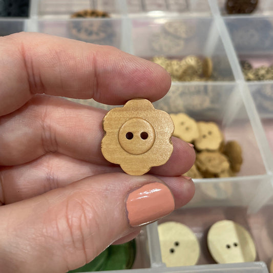 Hand holding a wooden button with a blurred background of a button collection container.