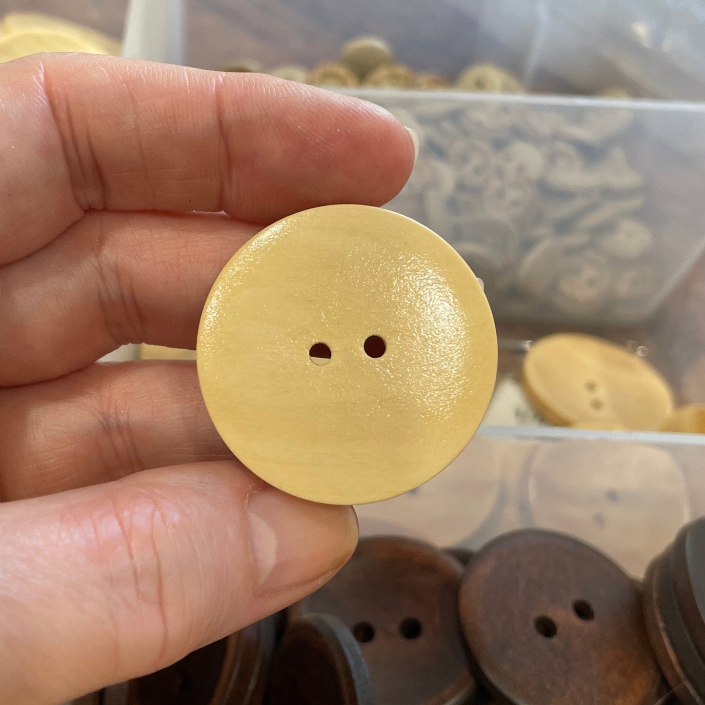 Hand holding a button with a clear container of buttons in the background
