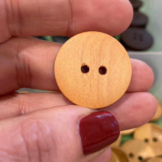Wooden button held between fingers with a container of buttons in the background
