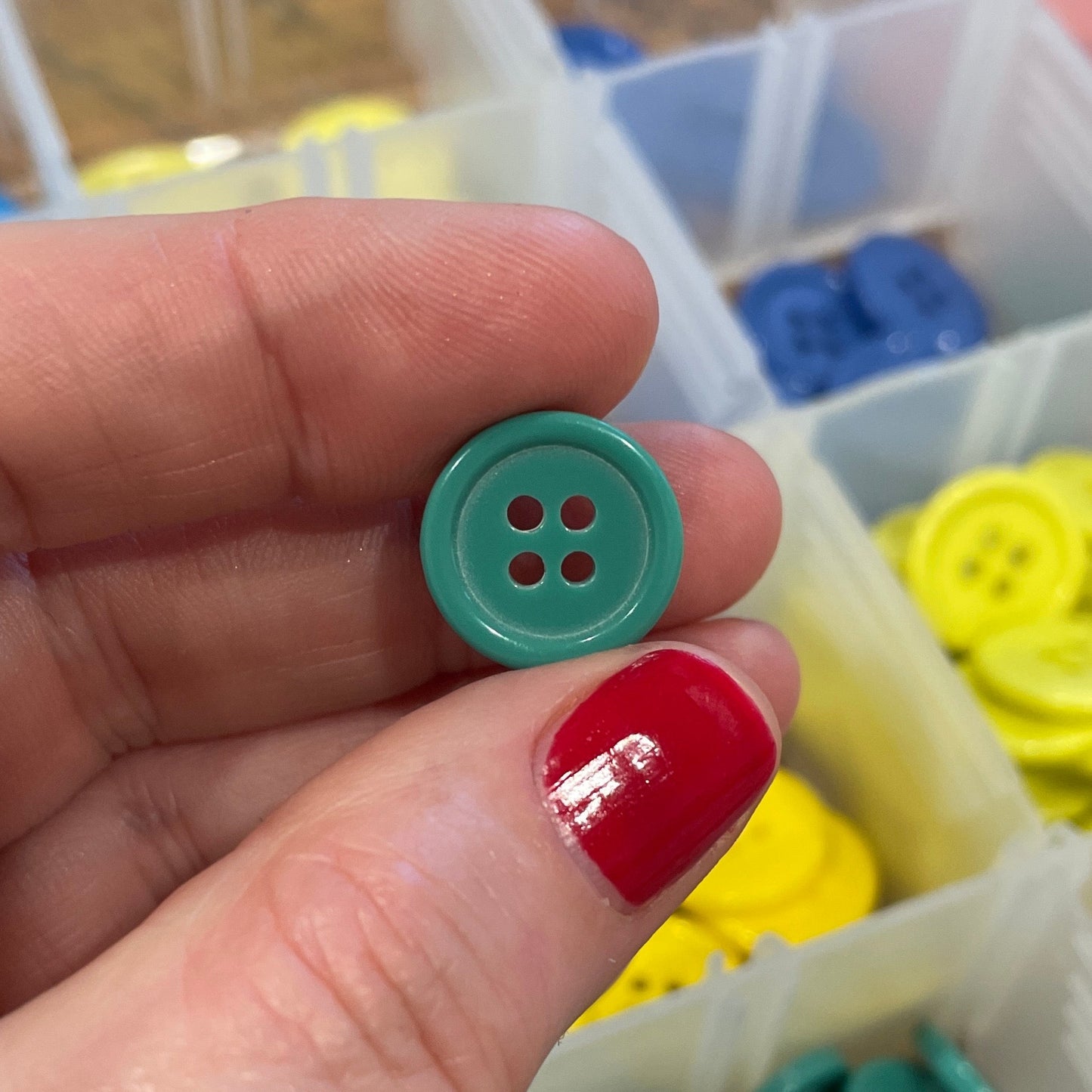 Hand holding a green button with a container of buttons in the background
