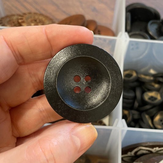 Hand holding a black button with a decorative center against a background of various buttons.