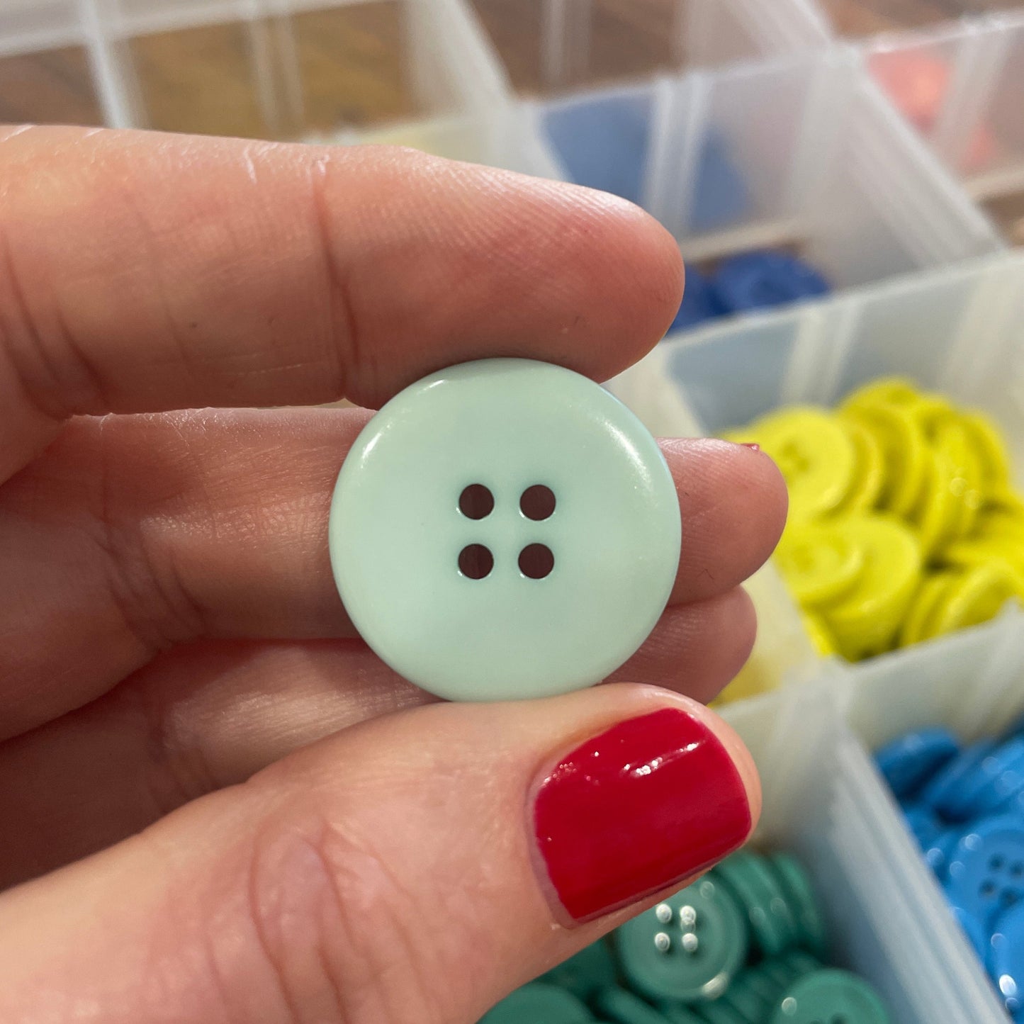 Hand holding a light green button with colorful buttons in the background