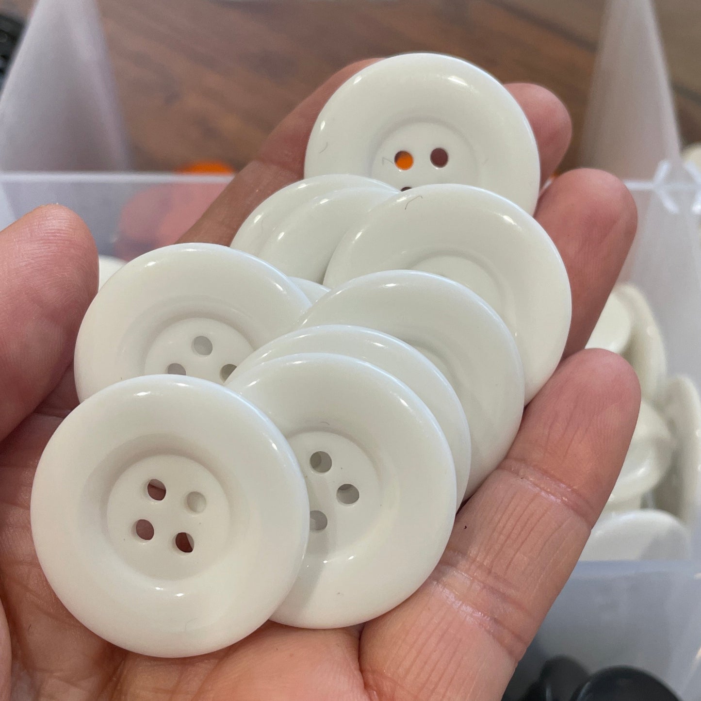 Hand holding white buttons with a blurred background of black buttons in a container.