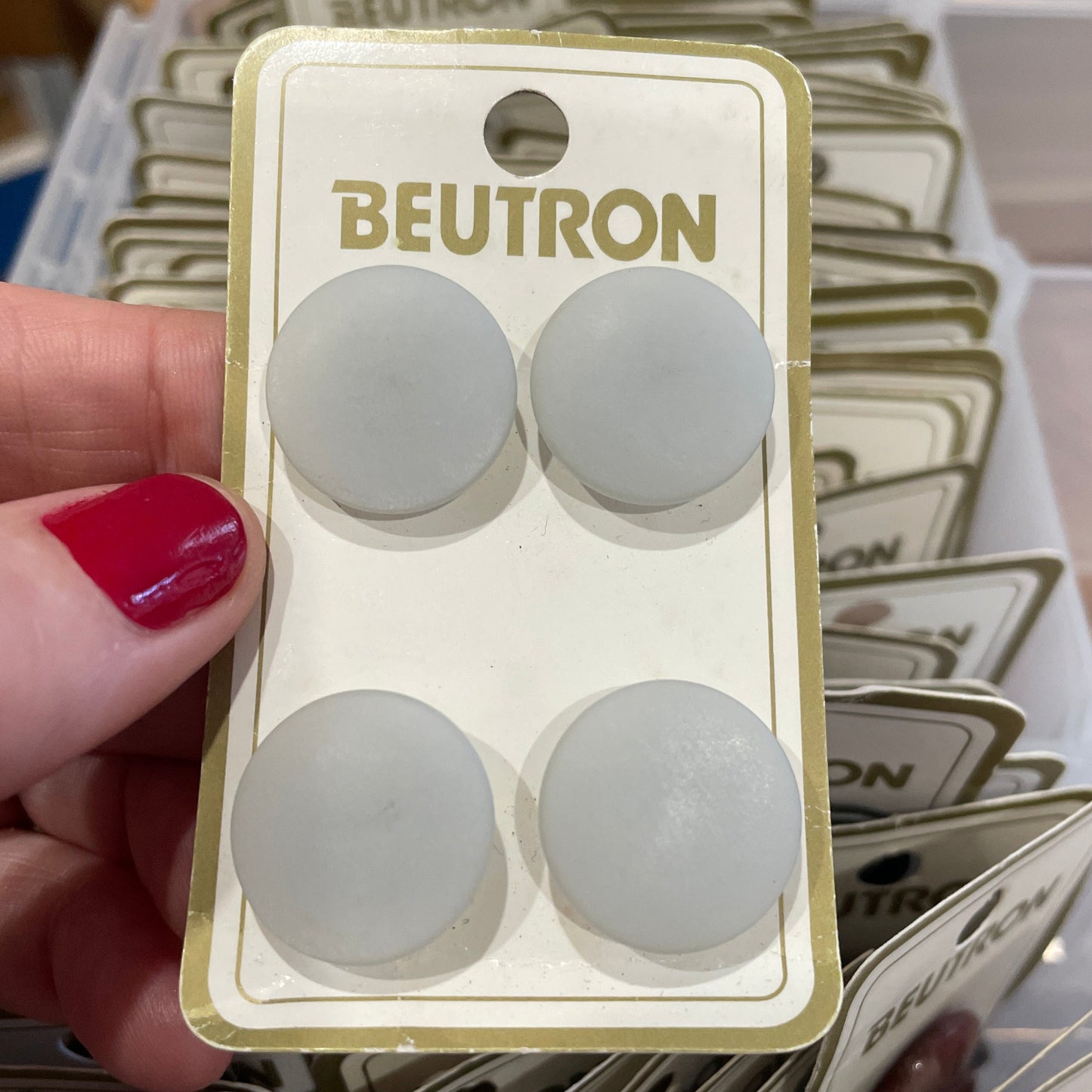 Pack of BEUTRON buttons held by a hand with red nail polish, surrounded by similar packaging.