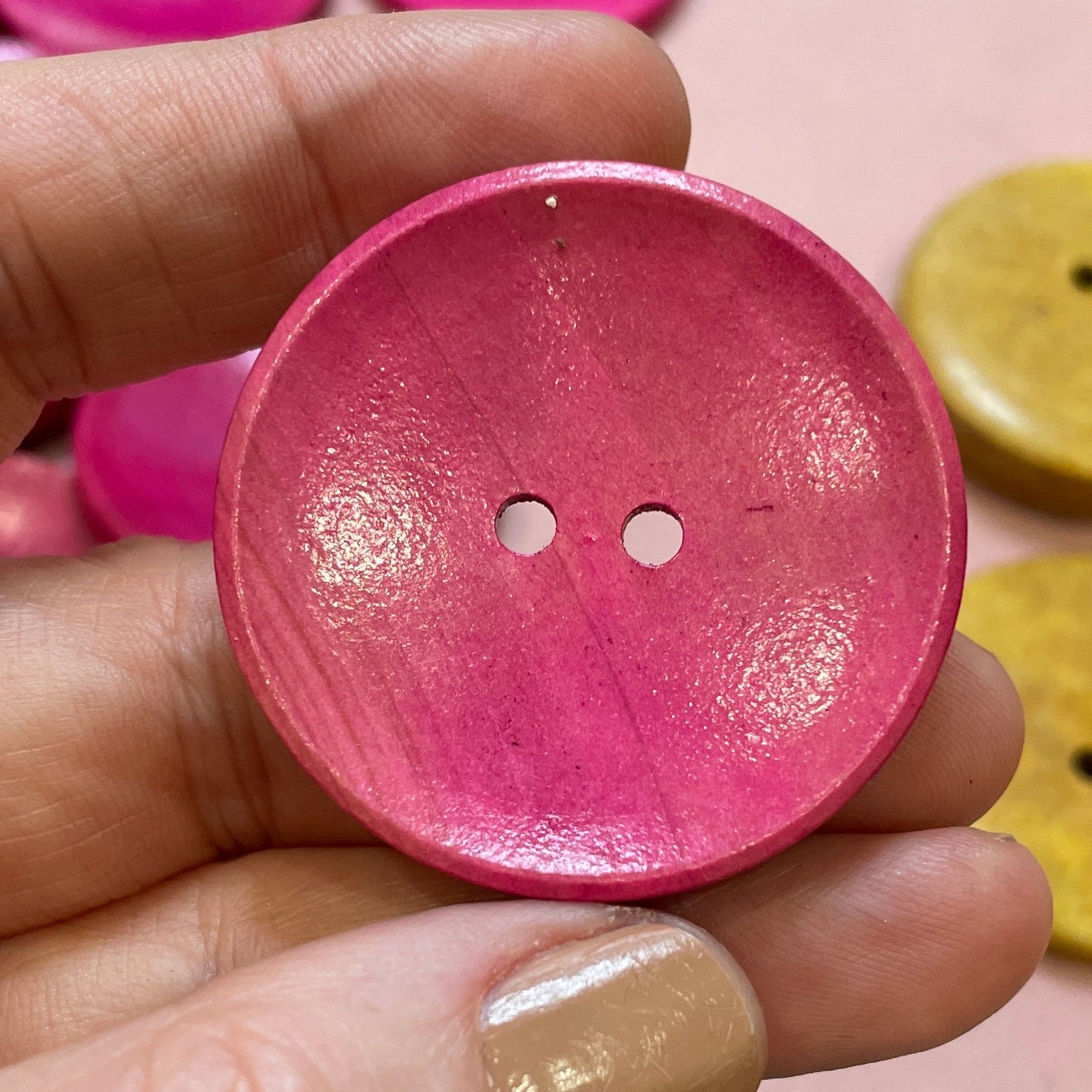 Hand holding a pink button with colorful buttons in the background