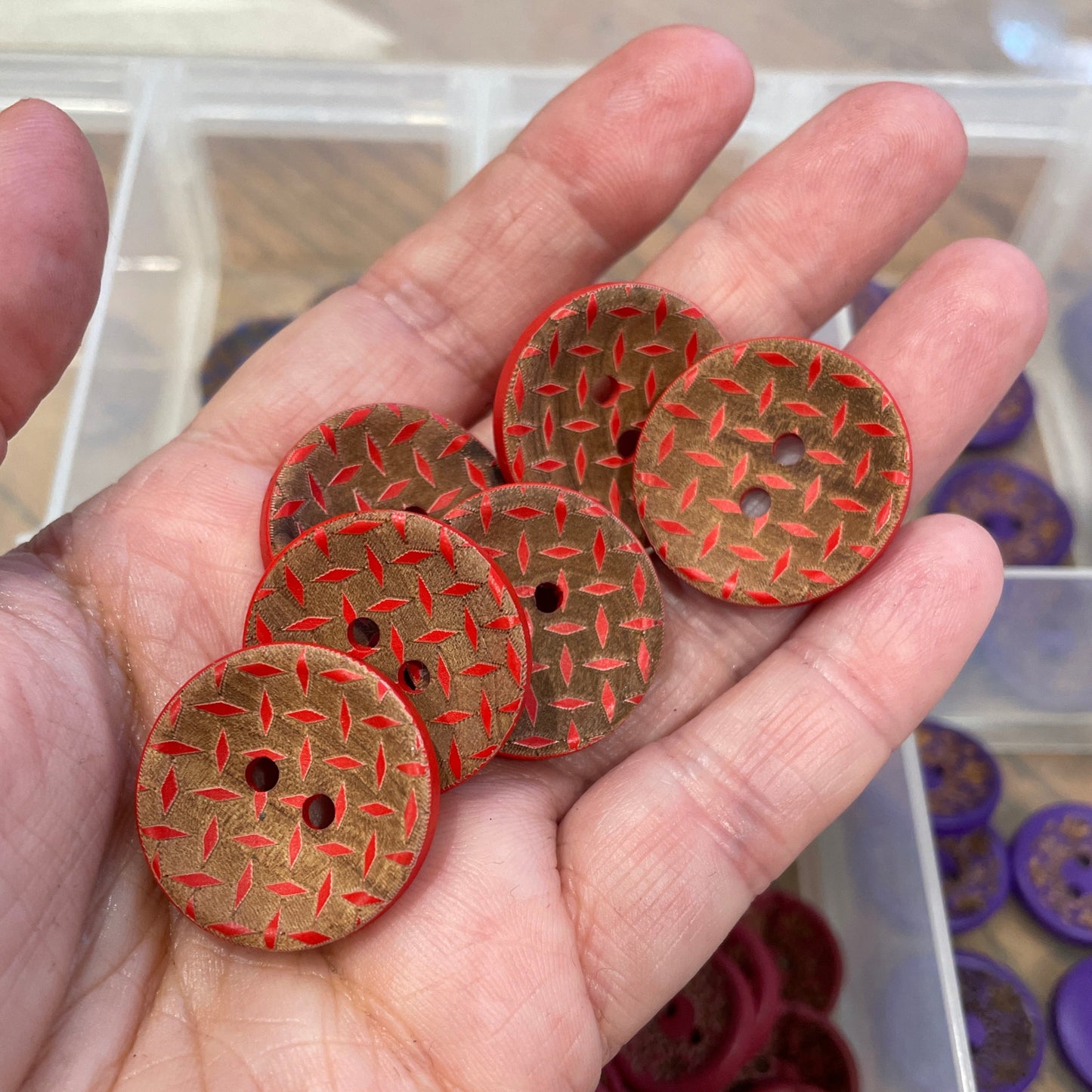 Hand holding red patterned buttons with a container of buttons in the background