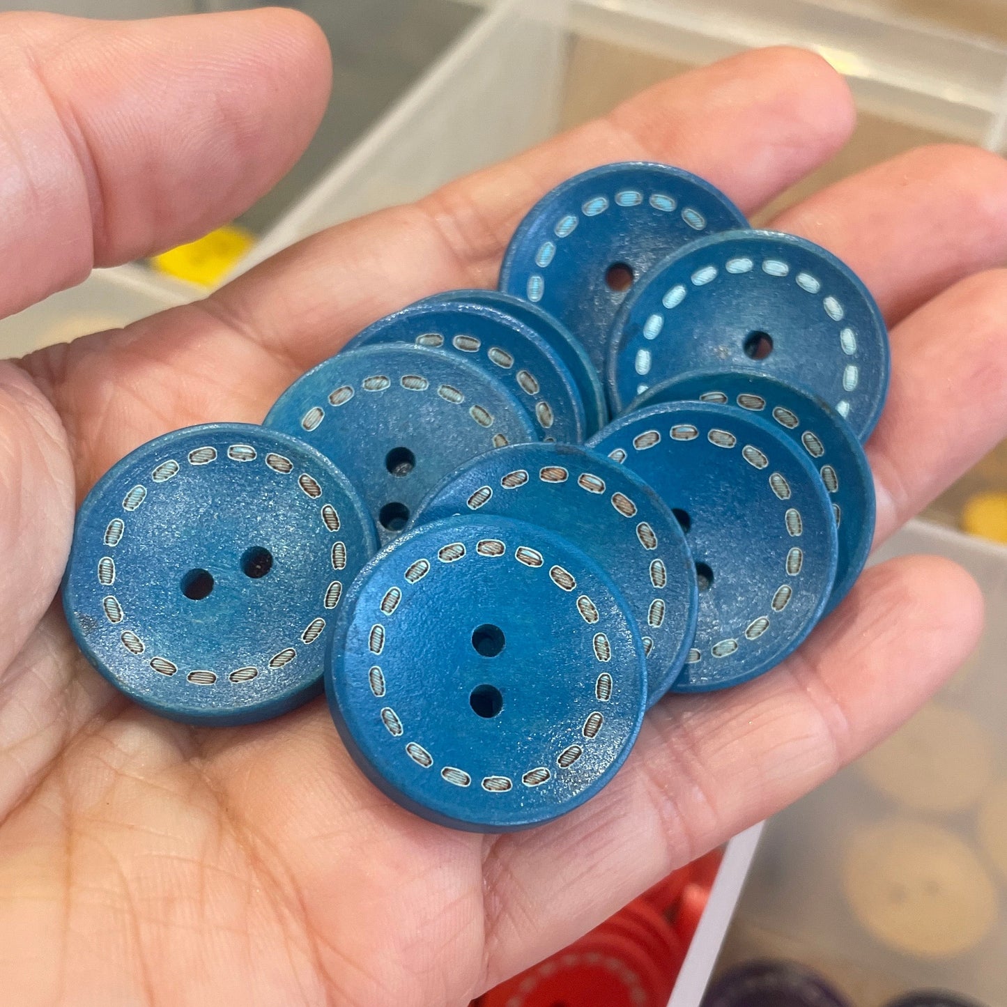 Hand holding blue buttons with a background of assorted buttons