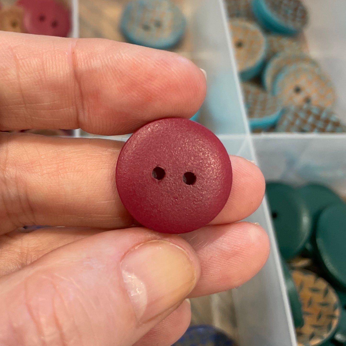 Hand holding a red button with a container of buttons in the background
