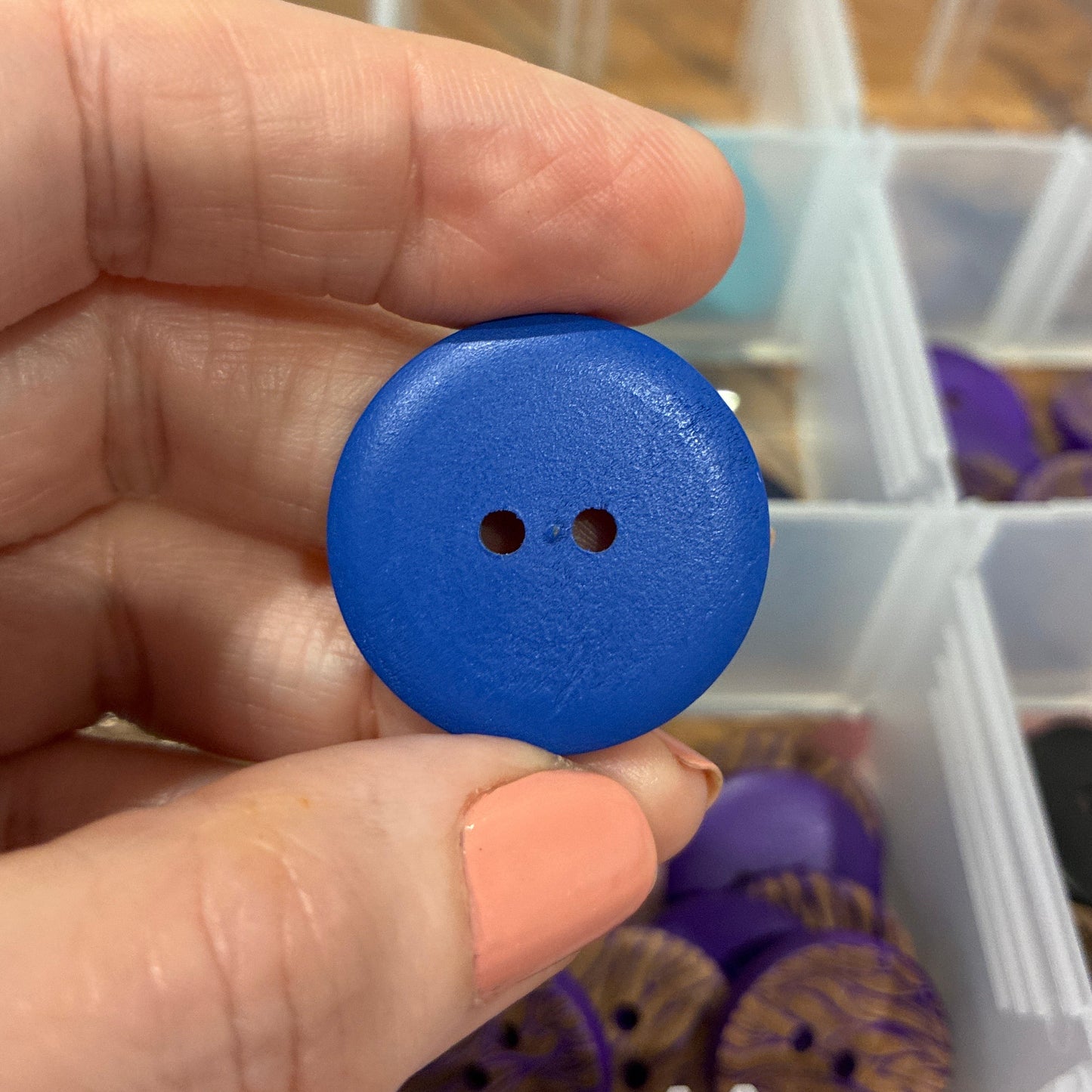Hand holding a blue button with a clear container of buttons in the background
