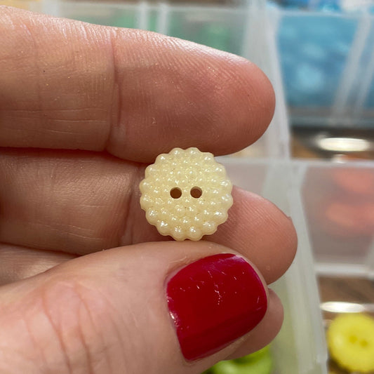 Hand holding a small white button with a blurred background of button containers.