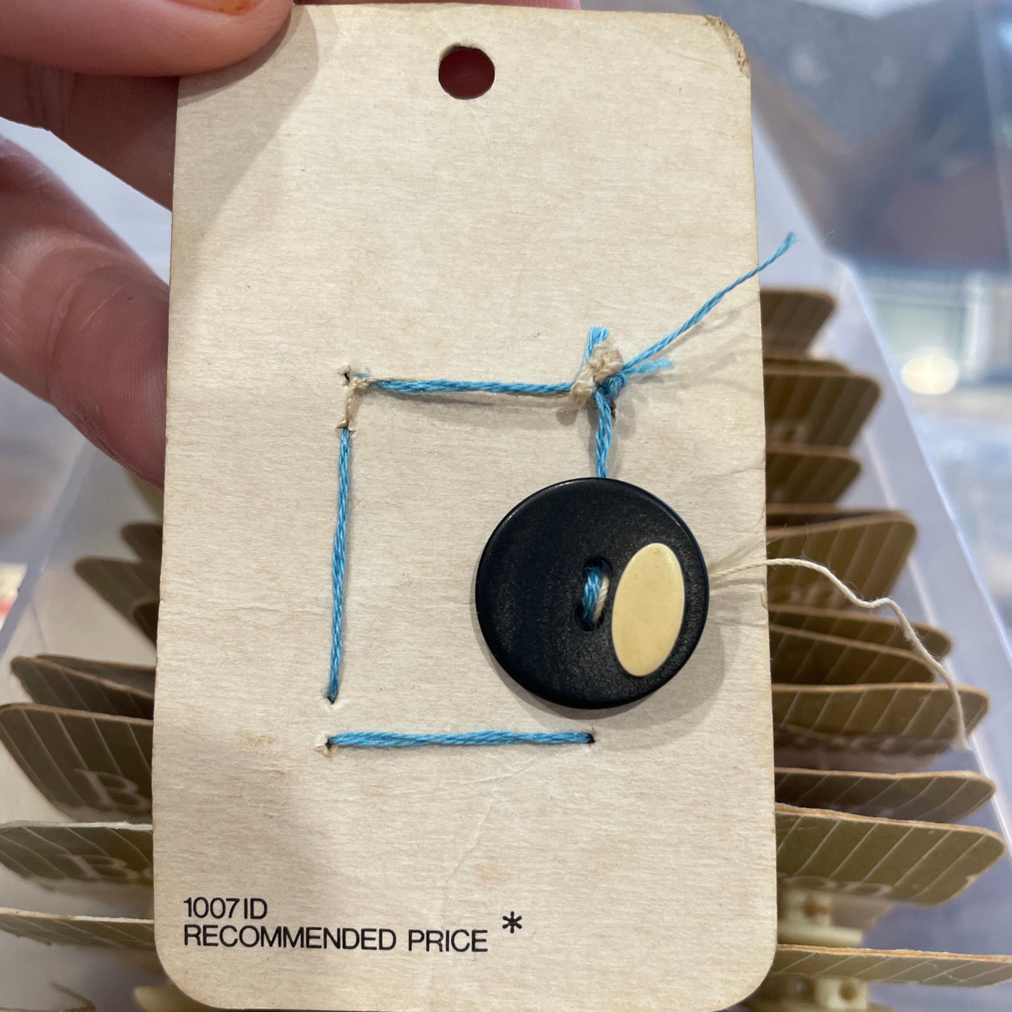 Close-up of a hand holding a Button with blue thread, against a blurred background.