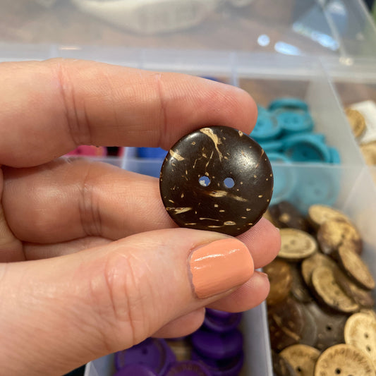 Hand holding a decorative button with a container of buttons in the background