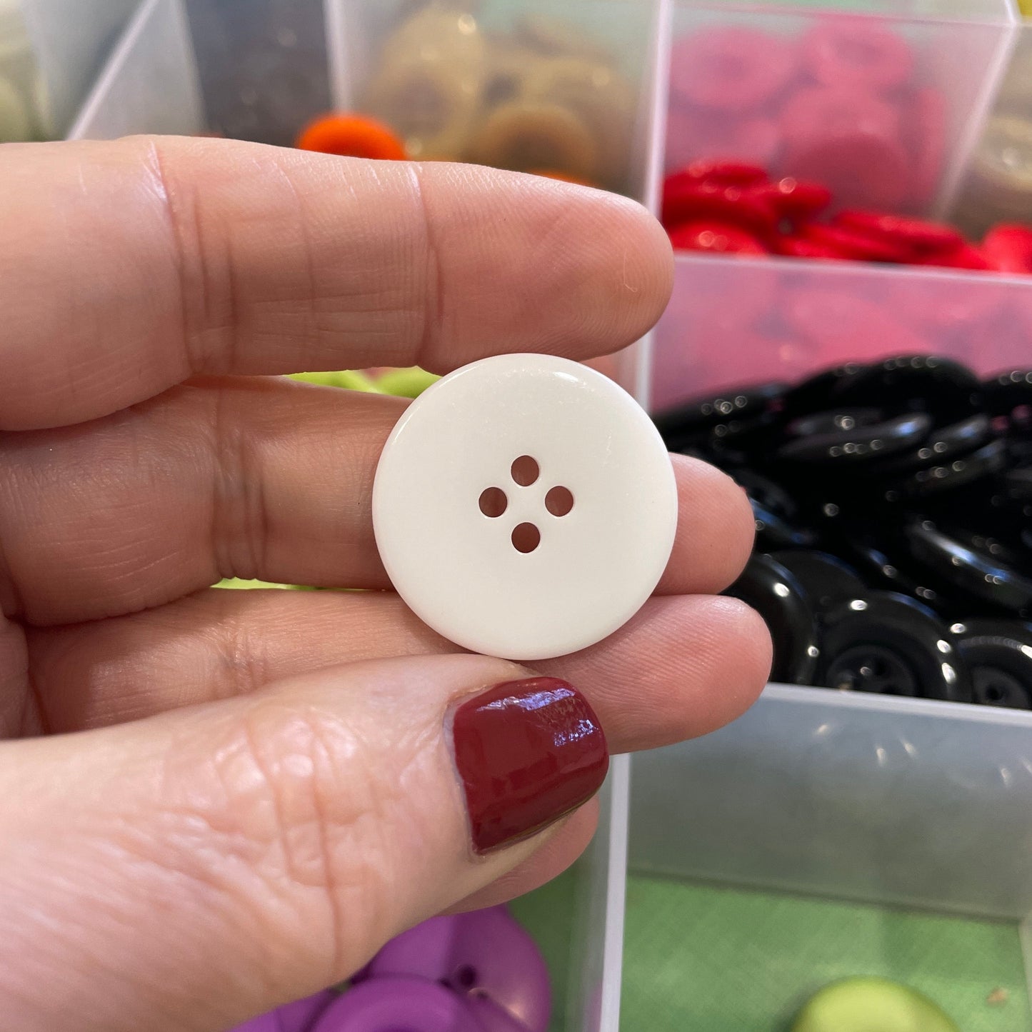 Hand holding a white button with a button collection in the background