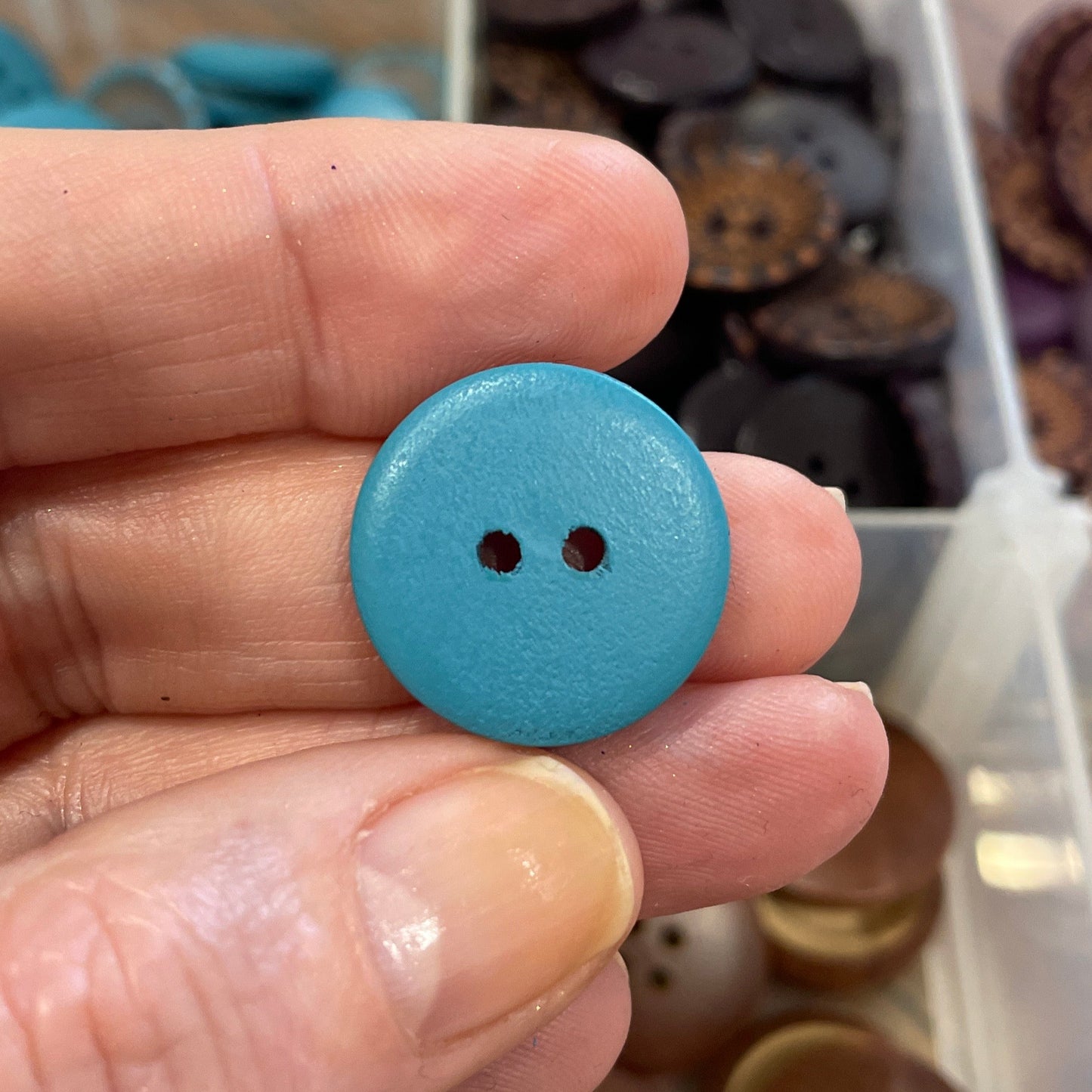 Hand holding a blue button with a clear container of buttons in the background