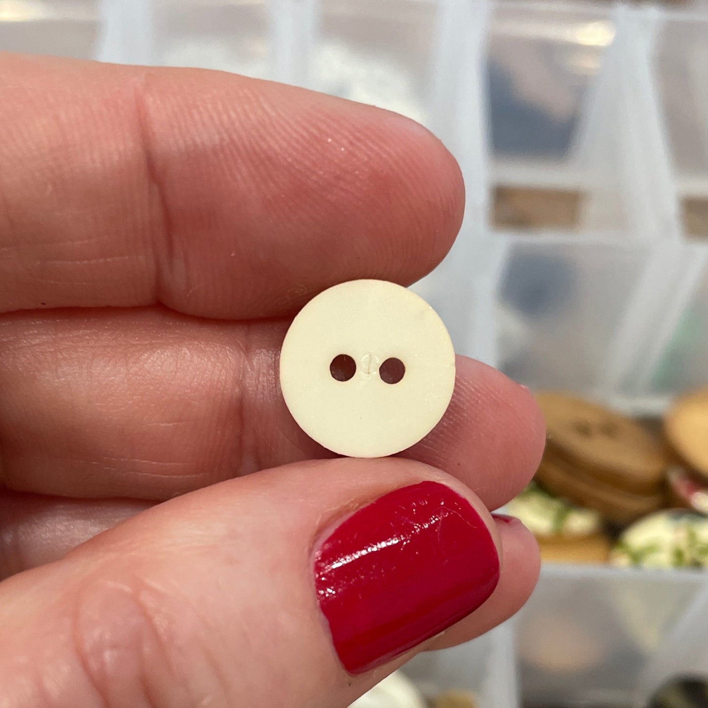 Hand holding a small gold button with a blurred background of a button collection.