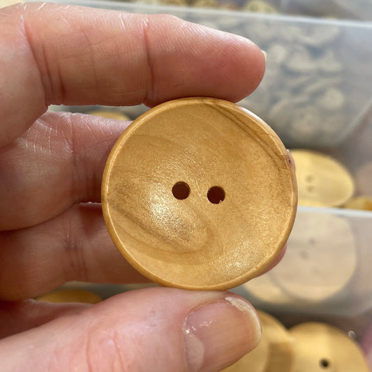 Button held between fingers with a clear container of buttons in the background