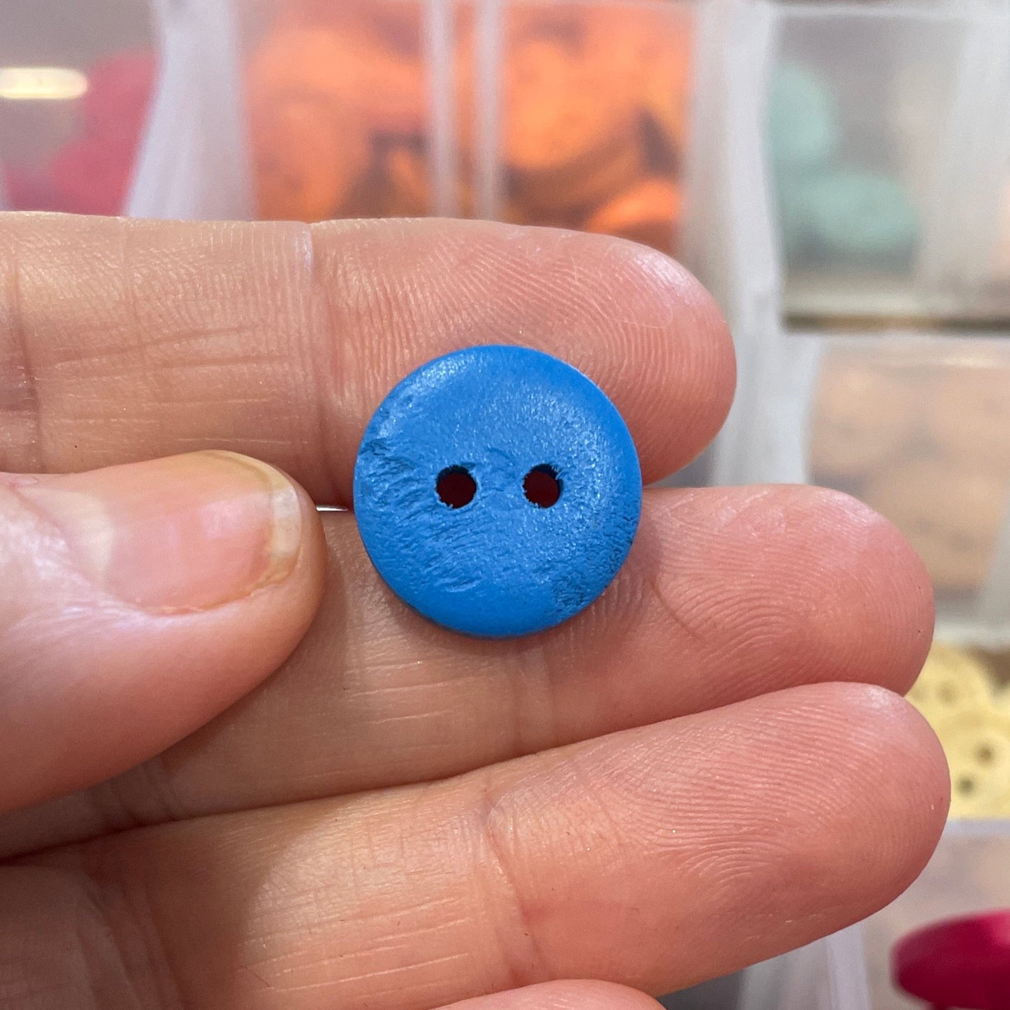 Hand holding a blue button with a container of colorful buttons in the background
