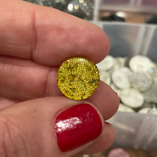 Gold glittery round object held between fingers with a blurred background of colorful items.