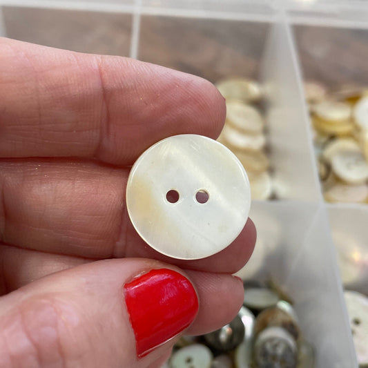 Hand holding a white button with a blurred container of buttons in the background