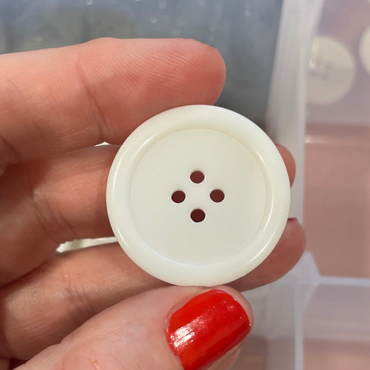 Hand holding a white button with a clear container of buttons in the background