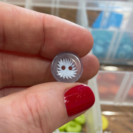 Hand holding a small metal object with a detailed design, against a background of a container with various buttons.