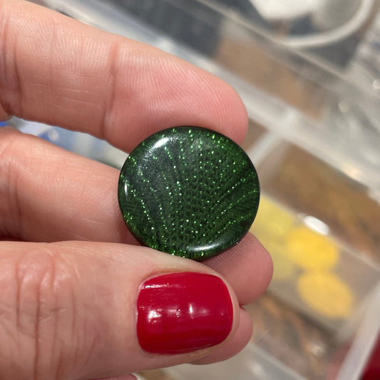 Hand holding a green button with a blurred background of button collection