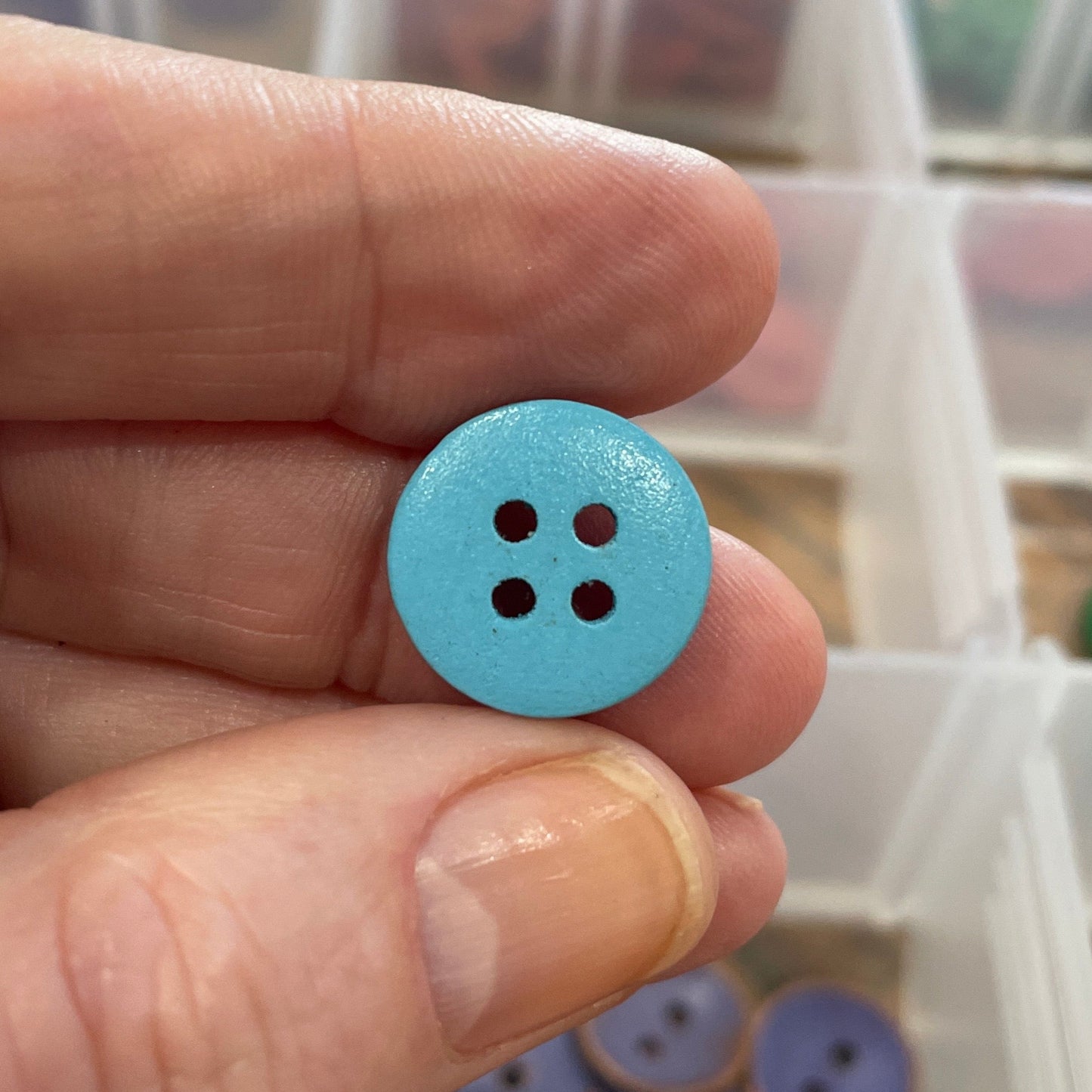 Hand holding a blue button with a blurred background of button containers.