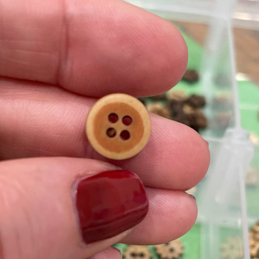 Hand holding a small yellow button with a blurred background of buttons in a container.