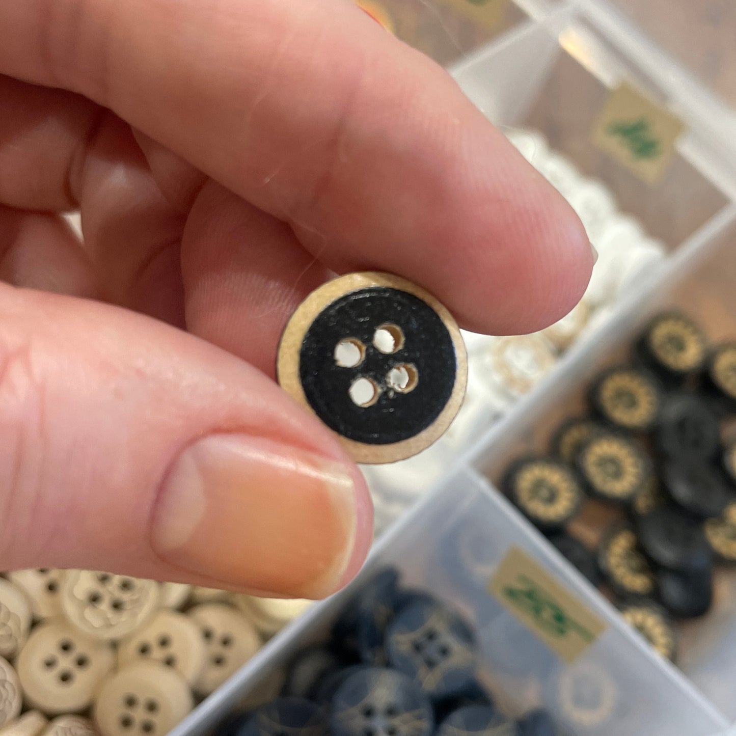 Hand holding a black button with a blurred background of button collection