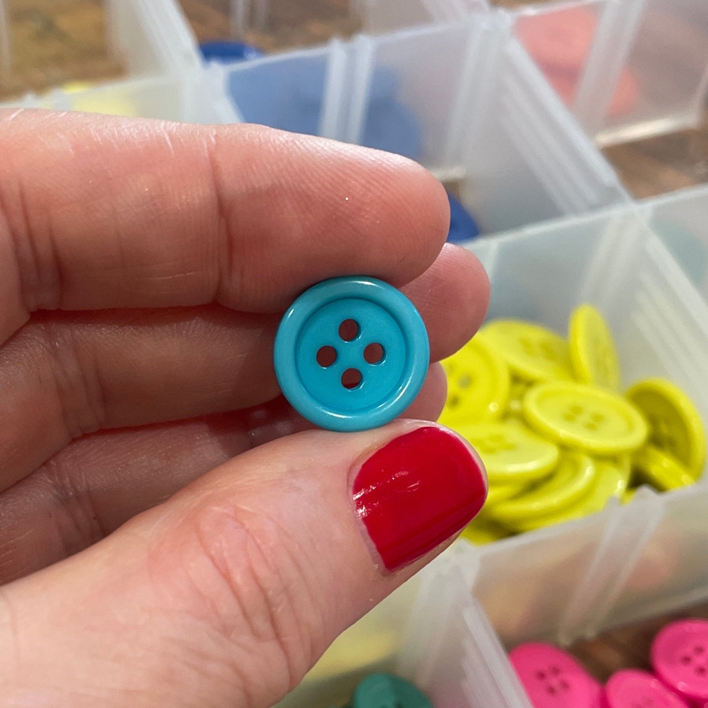 Hand holding a blue button with a container of colorful buttons in the background