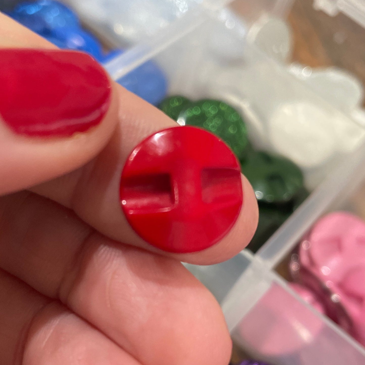 Hand holding a red button with a container of various buttons in the background