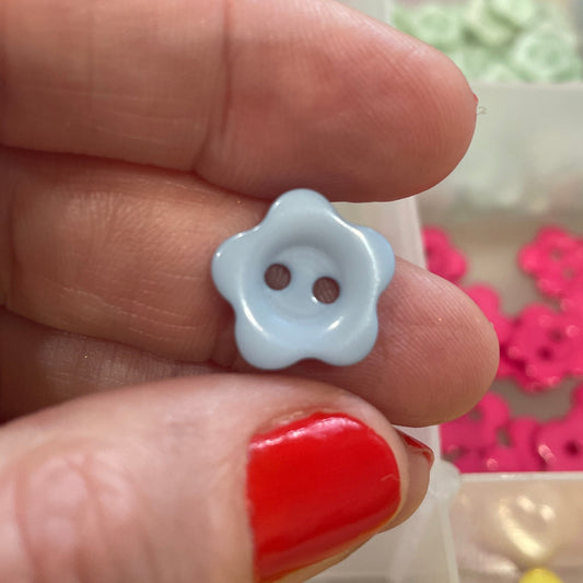 White flower-shaped button held between fingers with a container of colorful buttons in the background.