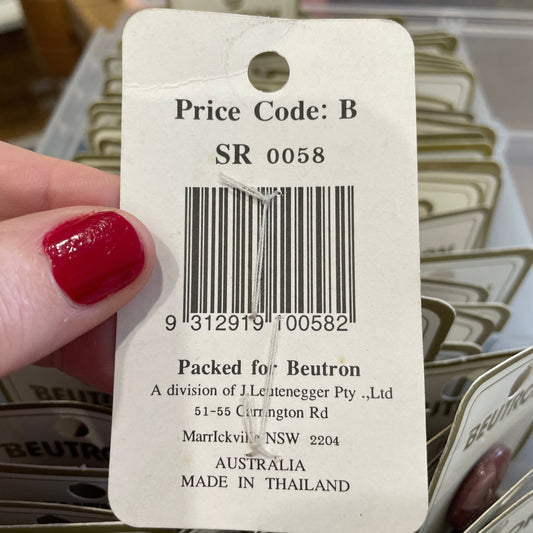 Close-up of a price tag with a barcode and text, held by a hand with red nail polish.