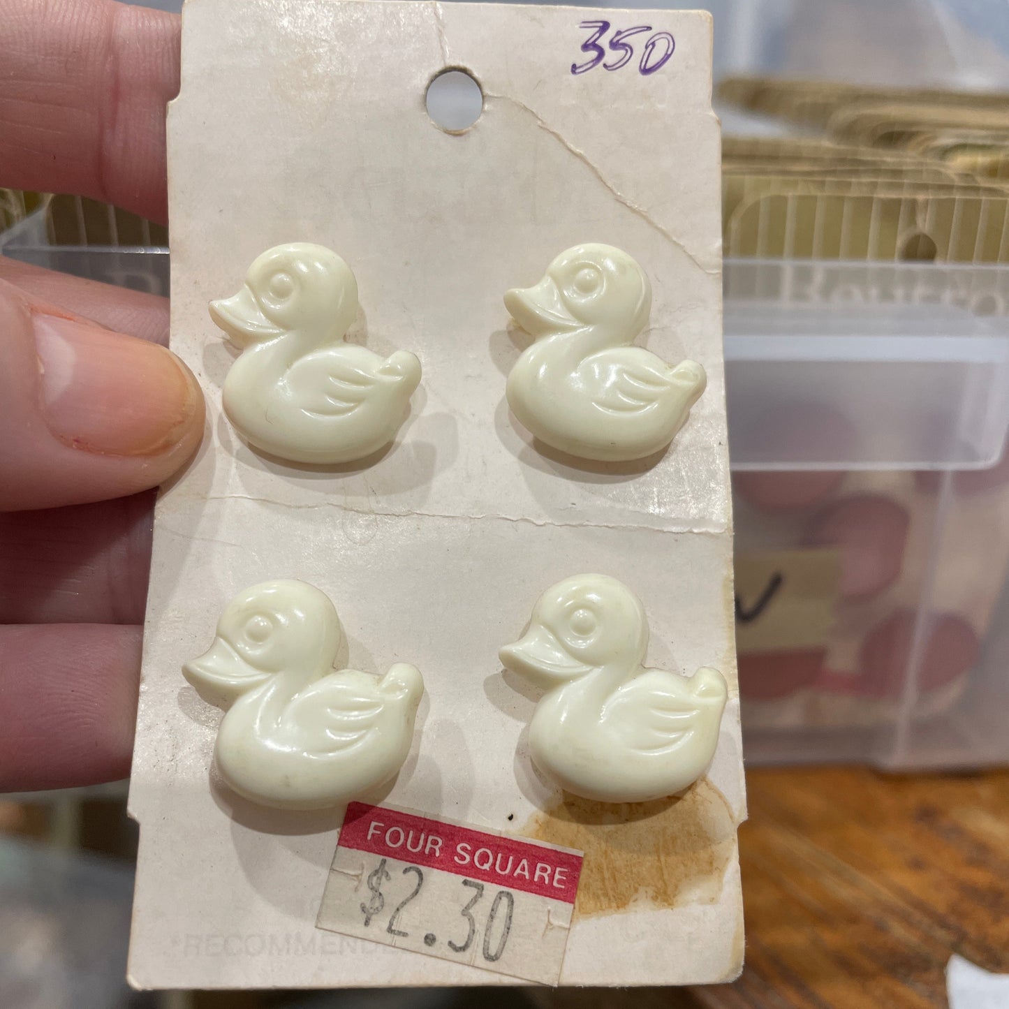 Four white duck-shaped buttons on a card with a price tag held by a hand.
