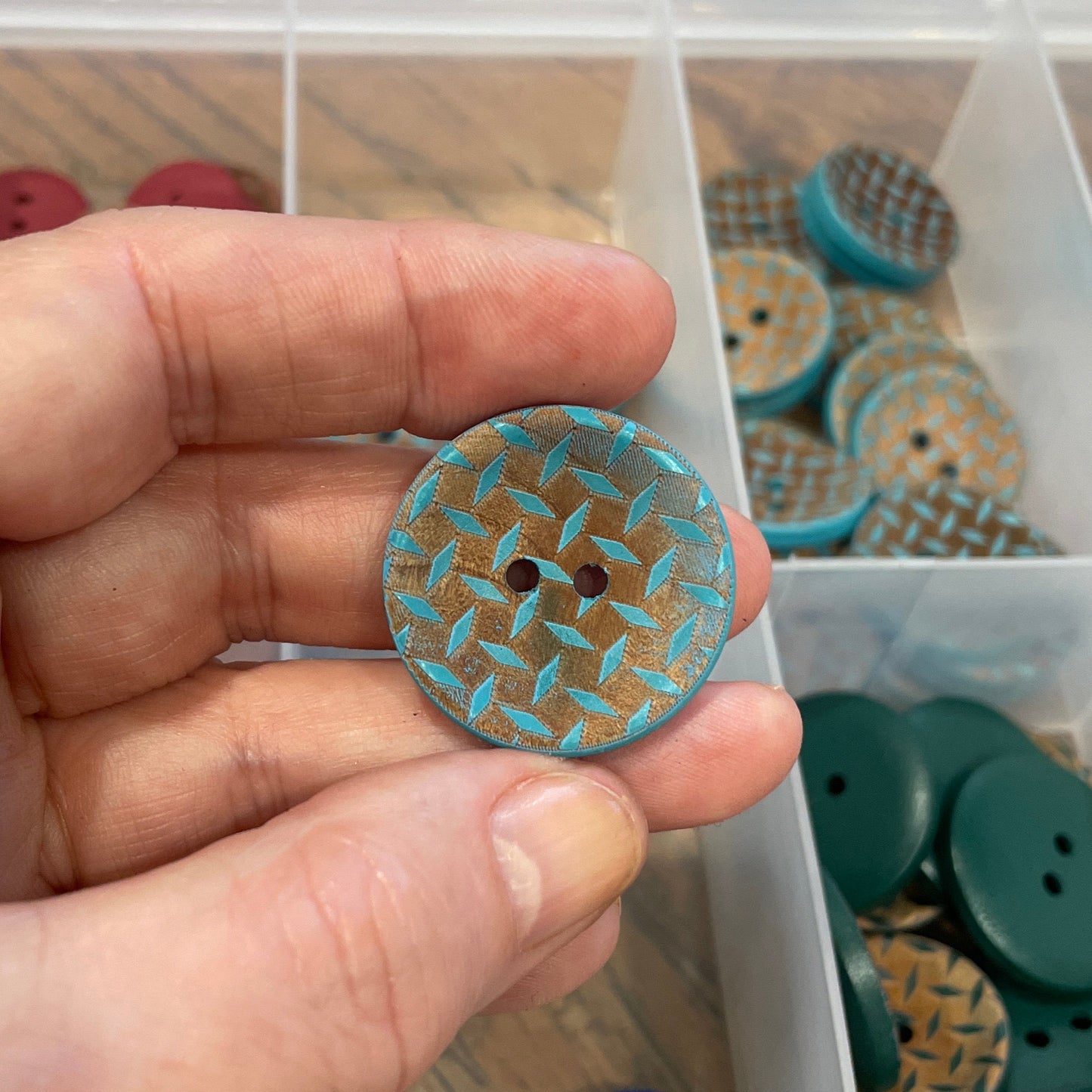 Hand holding a button with a clear container of assorted buttons in the background