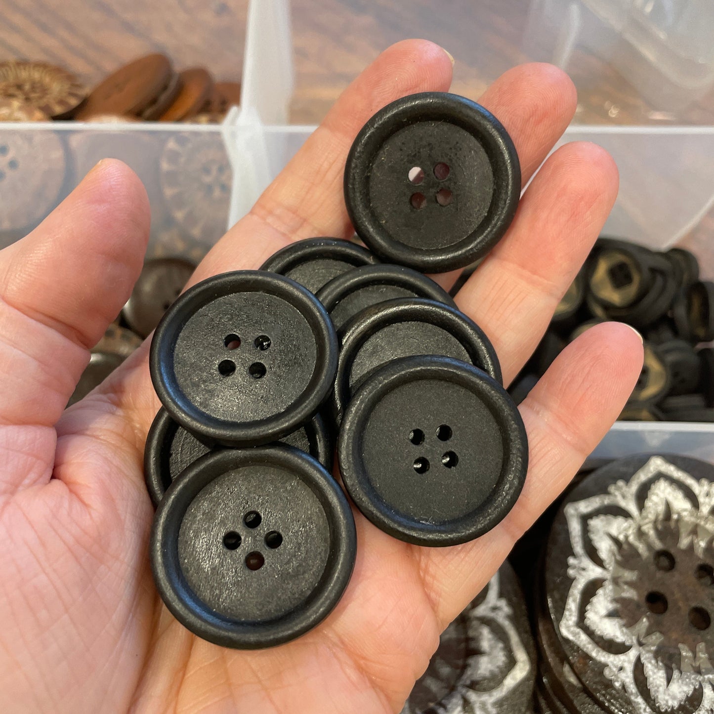 Hand holding black buttons with a clear container of buttons in the background