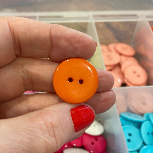 Hand holding an orange button with a container of colorful buttons in the background