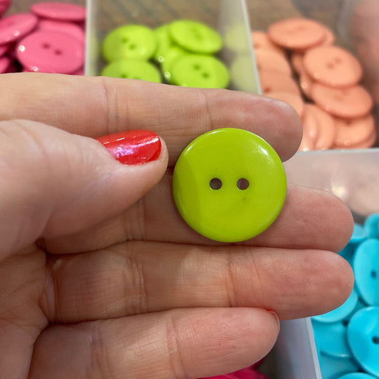Hand holding a green button with a background of colorful buttons in a drawer.