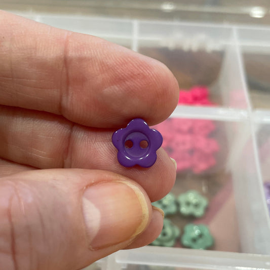 Hand holding a purple flower-shaped object with a container of colorful flower-shaped objects in the background.