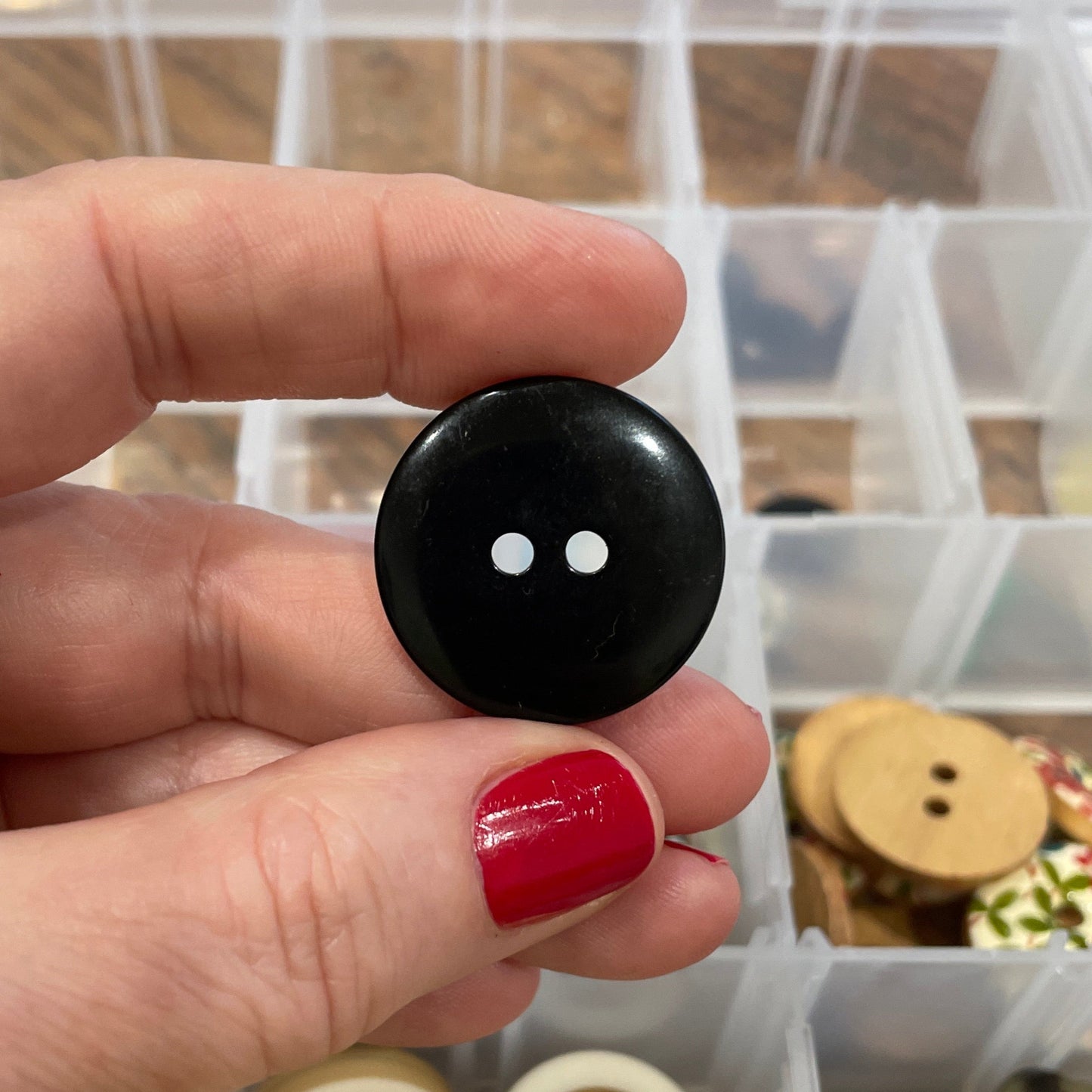 Hand holding a black button with a collection of buttons in the background