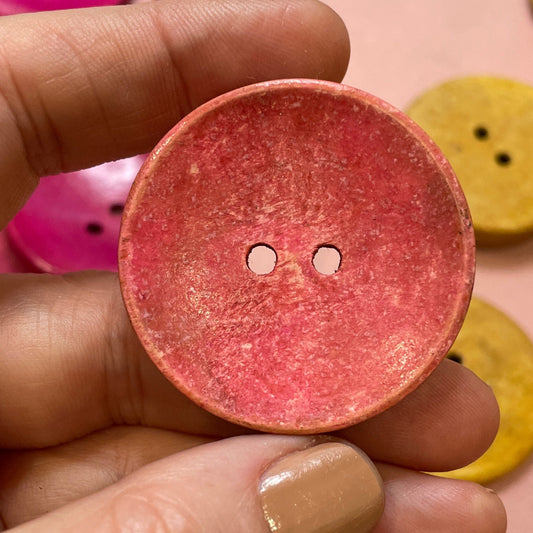Hand holding a pink button with other buttons in the background