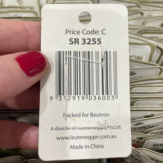 Close-up of a product tag with a barcode and text, held by a hand with red nail polish.