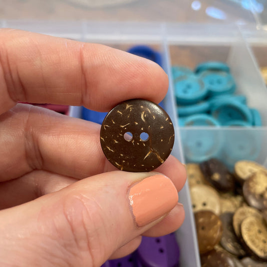 Hand holding a brown button with a clear container of buttons in the background