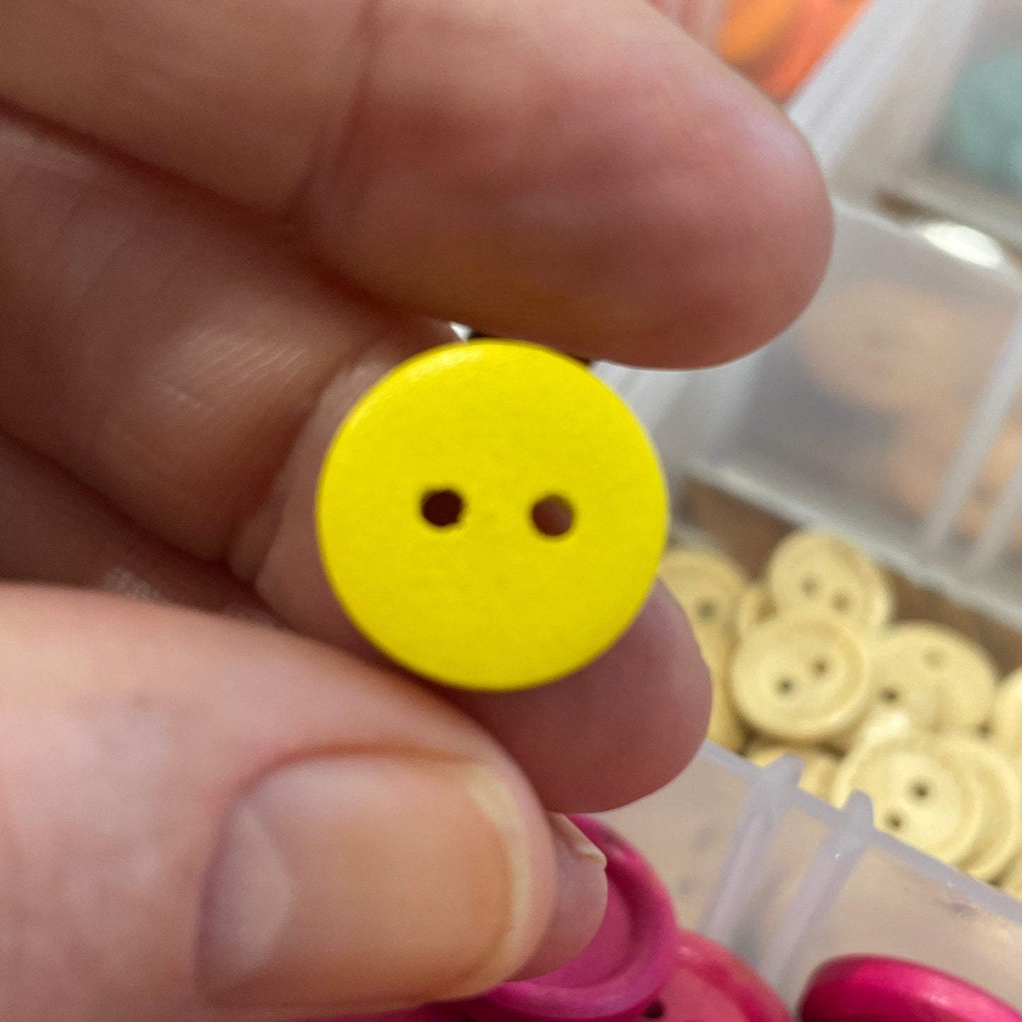 Yellow button held by a hand with pink buttons in a container in the background