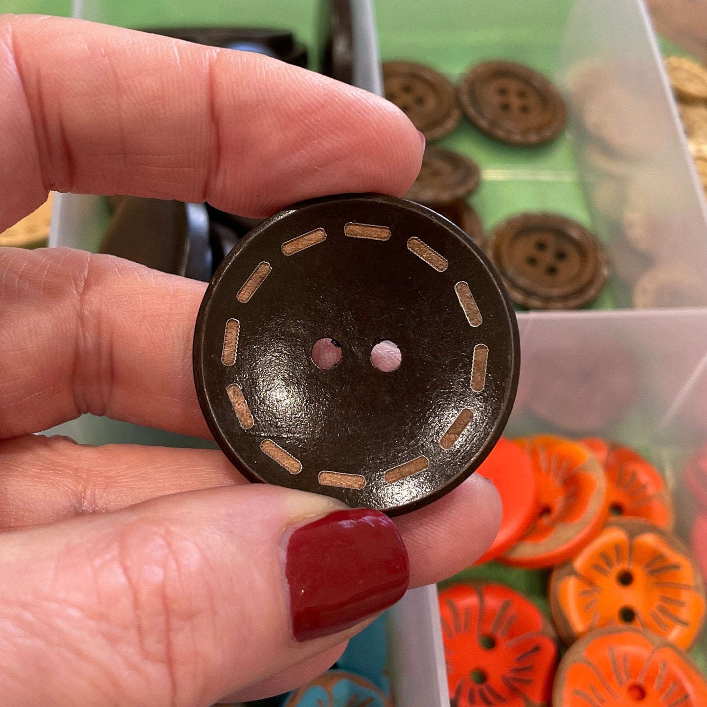 Hand holding a black button with a collection of colorful buttons in the background.