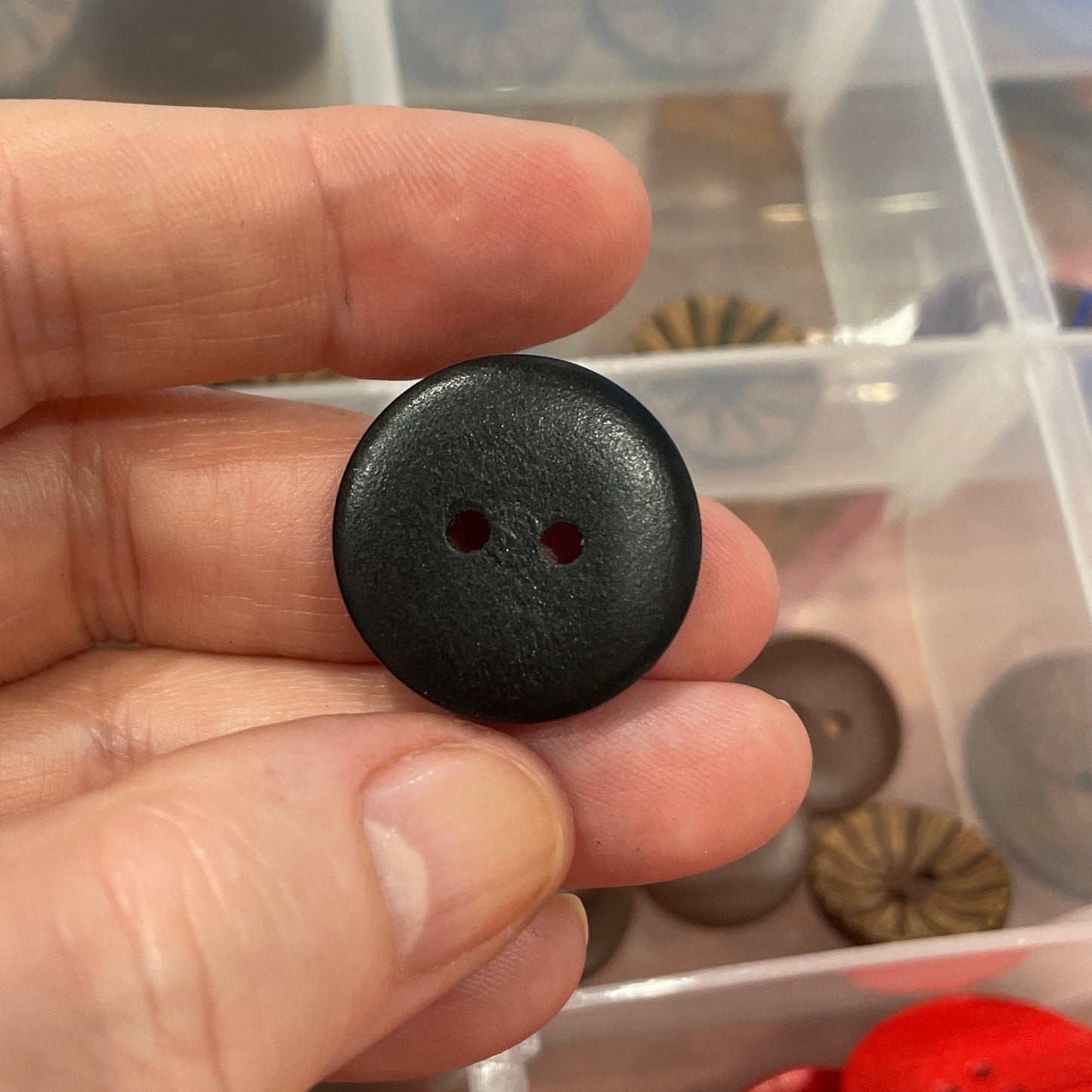 Black button held by a hand with a container of various buttons in the background