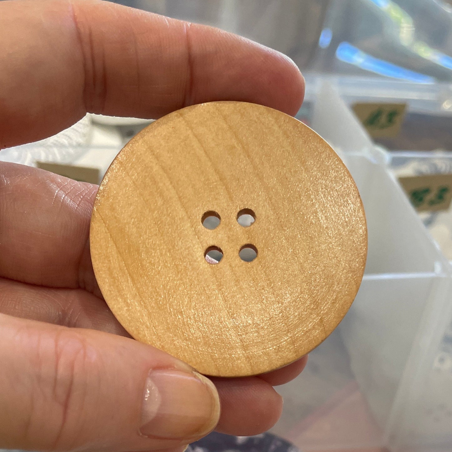 Hand holding a gold button with a clear plastic organizer in the background