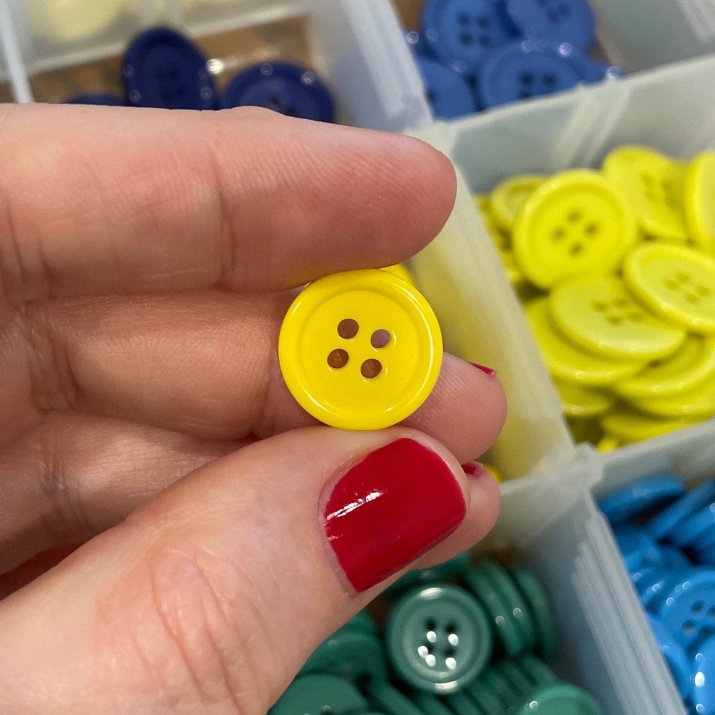 Hand holding a yellow button with containers of colorful buttons in the background