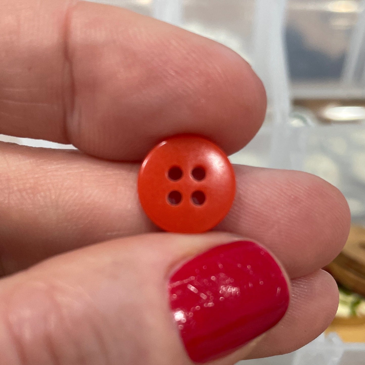 Hand holding a red button with a blurred background of button collection
