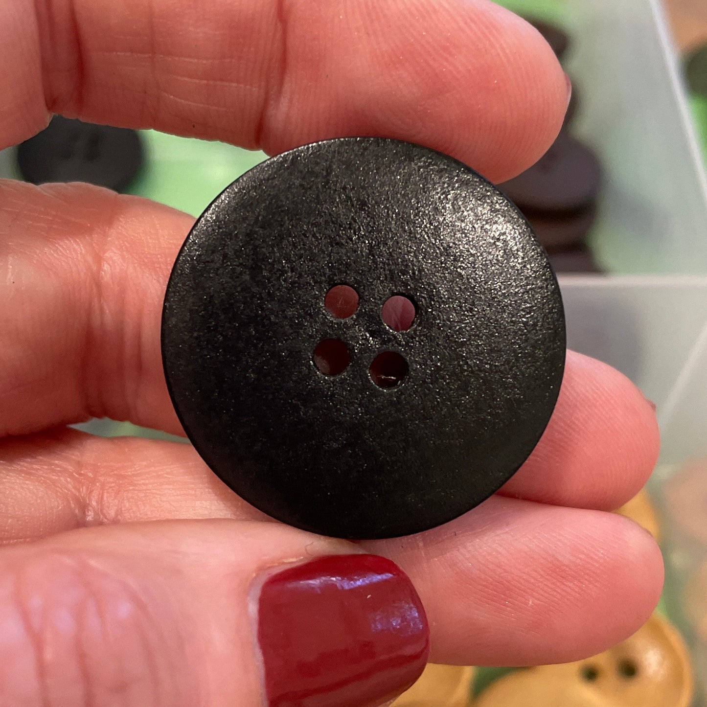 Black button held by a hand with a container of buttons in the background